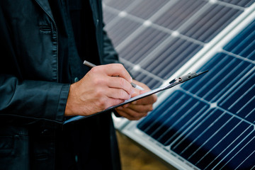 Closeup man write notes on clipboard beside solar battery