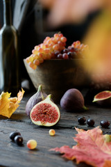 Fall still life. Ripe figs, grapes and yellow leaves. Dark wood background