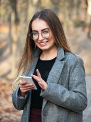 Portrait of beautiful young blonde woman enjoying warm day using her mobile phone in the autumn city park