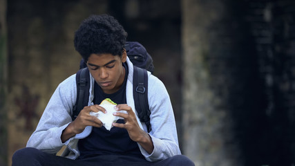 Lonely teenager holding sandwich sitting outdoors, having snack, solitude