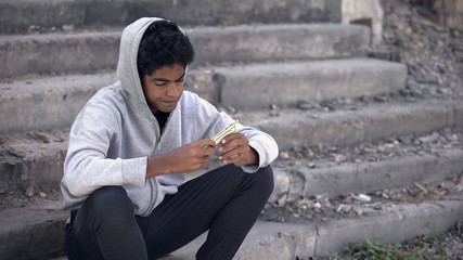 Disappointed black young man thinking of money sitting alone stairs, poverty