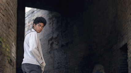 Naklejka na ściany i meble Black troubled teenager hanging around city building looking around, sadness