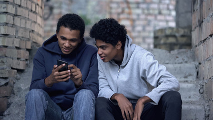 Teenagers sitting in abandoned house watching exciting video on smartphone