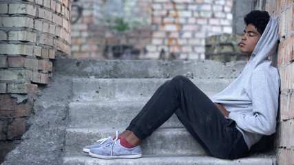 Homeless tired male child sitting abandoned building stairs, running from home