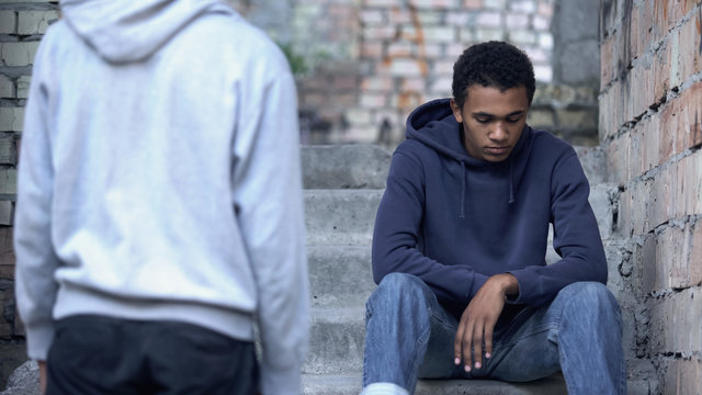 Young man looking at afro-american teenager sitting on stairs, trying to help