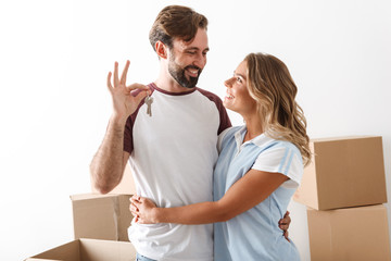Photo of smiling couple hugging near cardboard boxes and holding keys