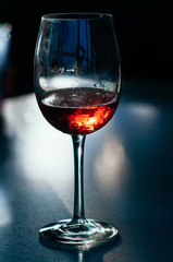 A glass of red wine on the table on dark blue background. Wine in a fogged up glass on a bar table, beautiful flecks and reflections from back light. Party, event, wine tasting, lounge concept