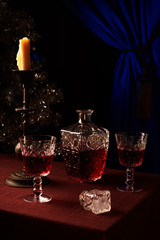 New Year's festive evening. Red wine is poured in crystal glasses. Decanter with red wine. The melted-off candle in an ancient lamp-stand. Christmas tree decorations. Quiet relaxed atmosphere for love