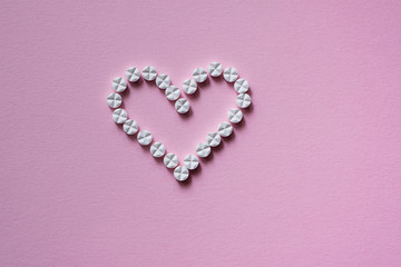 Heart sign made of medicine pills on a pink background. Isolated.