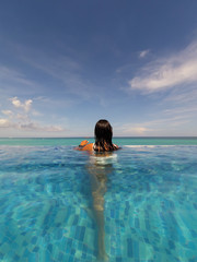 Rear view of a brunette woman in swimming pool looking at sea
