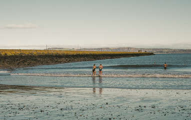 dwie kobiety w strojach kąpielowych wchodzą do zimnego morza podczas jesieni