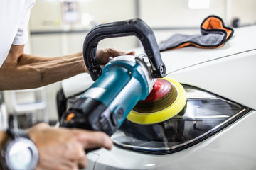 Car detailing - Hands with orbital polisher in auto repair shop. Selective focus.