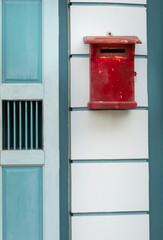 An old wood mailbox is untidy painted by red colour. It's hang on wall near old asian style light green door.