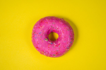 Sweet pink donut decorated with colorful icing isolated on yellow background. Bright tasty bun. Minimal summer concept. Copy space. Flat lay. The concept of not healthy eating and weight gain