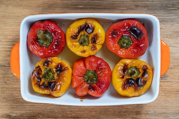 Baked red and yellow bell peppers. Peppers in a baking dish on a wooden table. A healthy and delicious vegetarian dish. Closeup, top view