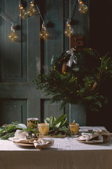 Christmas or New year table setting with empty ceramic plates, napkins, Christmas thuja wreath, luminous garland and burning candles on white tablecloth. Holiday mood