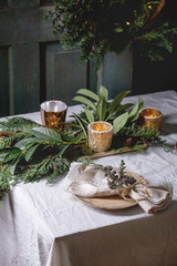 Christmas or New year table setting with empty ceramic plates, napkins, Christmas thuja wreath, luminous garland and burning candles on white tablecloth. Holiday mood
