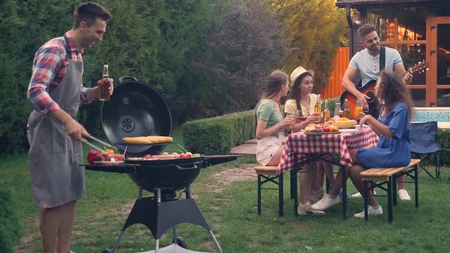 Young man cooking delicious food on grill for his friends at barbecue party outdoors. Picnic time