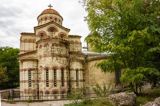 Church St. John Baptist, built in 8th century against cloudy sky. Closeup temple building built and Crimean stone. On bell tower and domes church Orthodox crosses.