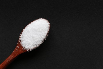 Sea salt in wooden spoon on black background with copy space