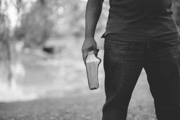 Closeup shot of a male holding the bible with a blurred background in black and white