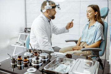 Fototapeta premium Senior otolaryngologist preparing for the medical examination procedure for a woman patient in the medical office with ENT workstation