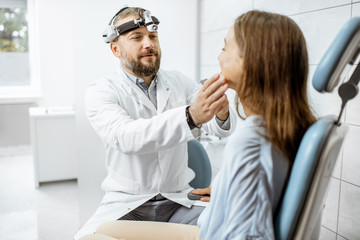 Obraz premium Senior otolaryngologist examining nose of a young patient during a medical examination in the ENT office