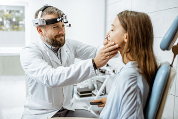 Senior otolaryngologist examining nose of a young patient during a medical examination in the ENT office