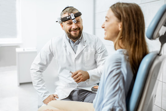 Portrait of a cheerful senior otolaryngologist during a medical consultation with a young patient in ENT office