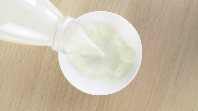 Pour milk from glass bottle into white bowl in slow motion. Food and drink closeup.
