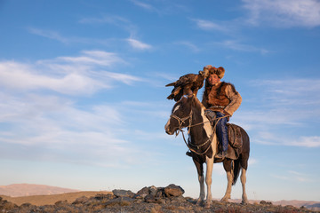 Naklejka premium Portrait of a traditional kazakh eagle hunter with his colorful horse and majestic golden eagle on a sunny day. Ulgii, Western Mongolia.