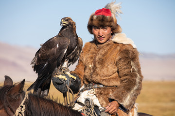 Portrait of a traditional kazakh eagle hunter with his golden eagle and horse. Ulgii, Mongolia.