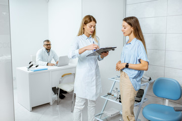 Young patient with female doctor during a medical consultation standing at the ENT office with senior doctor on the background