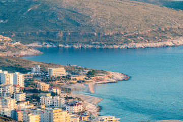 Golden hour landscape and cityscape from Lekuresi Castle, Saranda, Albania with Adriatic Sea coast and residential district view, clear spring sky with evening haze