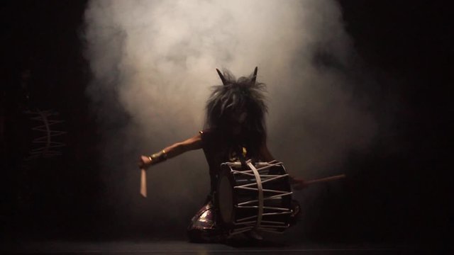 Four artists drummers Taiko in a wig with horns and make-up drum on stage against a dark background with smoke. Demons from Japanese mythology.