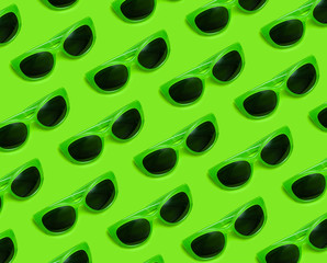Pattern of Stylish green sunglasses with black glasses on bright green background top view flat lay copy space. Fashion glasses, summer accessory, hipster, holiday vacation, minimal youth style