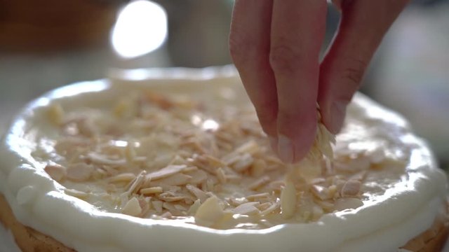 Woman baker puts nuts on a cake with cream.