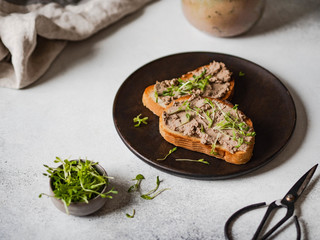Two toasts chicken rillettes (pate) on white bread with sprouts on dark wood plate on a light background . Copy space