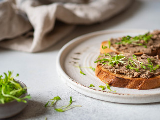 Two toasts chicken rillettes (pate) on white bread with sprouts on white plate on light background...