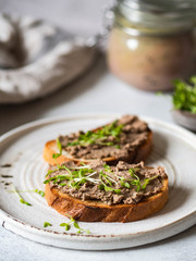 Two toasts chicken rillettes (pate) on white bread with sprouts on white plate on light background .