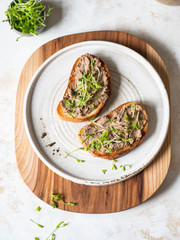 Two toasts chicken rillettes (pate) on white bread with sprouts on white plate on wood cutting...