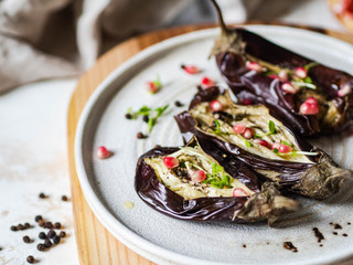 Baked eggplants slices with spices, sprouts, pomegranate and olive oil on a white ceramic plate on gray background.