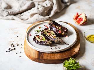 Baked eggplants slices with spices, sprouts, pomegranate and olive oil on a white ceramic plate on gray background.