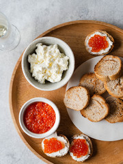 Fototapeta na wymiar Sandwiches with cream cheese and red caviar on a large wooden tray and ingredients in bowls