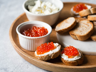 Sandwiches with cream cheese and red caviar on a large wooden tray and ingredients in bowls