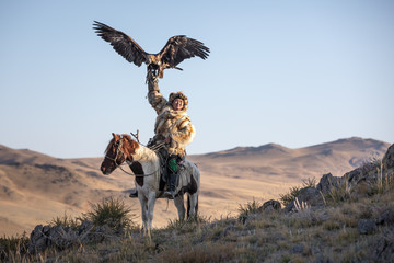 Old traditional kazakh eagle hunter posing with his golden eagle in the mountains. Ulgii, Western...