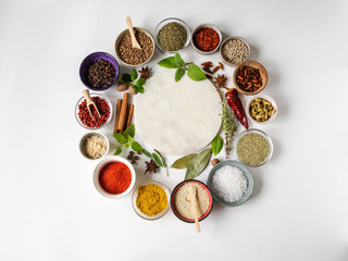 Fototapeta na wymiar Various dry spices and raw herbs frame flat lay in small bowls and wood cutting marble board in the center on white background. Top view, copy space