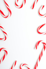 Blank frame with Christmas candy canes top view. New Year lollipops on white background. Winter holidays backdrop with copyspace. Xmas confection composition with decorative elements.