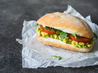 Vegan fast food sandwich with avocado mashed, tomatoes and arugula with white bun on a white paper