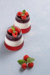 Berry jelly with raspberries in a glass cup on light blue background.